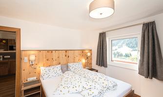 A cozy bedroom with a double bed and wood-paneled walls. Large windows let in plenty of daylight and offer a view of the landscape.