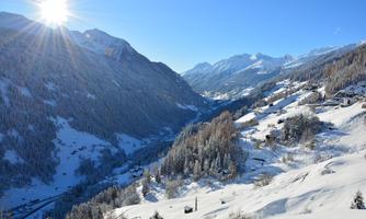 An impressive winter landscape with snow-covered mountains and a clear blue sky. The sun shines over the idyllic valley.