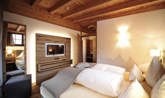 A modern bedroom with wooden ceilings and soft lighting. It is elegantly furnished with a double bed and a flat-screen TV.