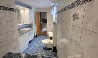 A modern bathroom with white tiles and blue accents. There is a bathtub, a toilet, and a view of the shower and the sink.