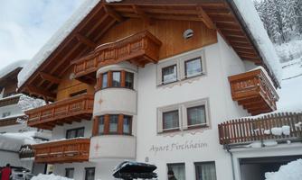 A charming house in alpine style, surrounded by plenty of snow. The facade is made of wood and has several balconies.