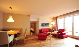 A modern living room with red sofas and a dining area. Large windows let in plenty of light and showcase a warm wooden floor.