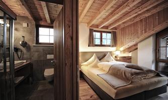 A cozy bedroom with a wooden ceiling and large windows. Next to the bed is a modern bathroom with a shower.