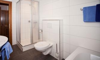 A modern bathroom with a shower and bathtub. White tiles and blue towels give the room a fresh touch.
