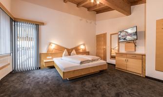 A modern bedroom with wood decor and a large bed. The room has a cozy atmosphere and a TV on the wall.