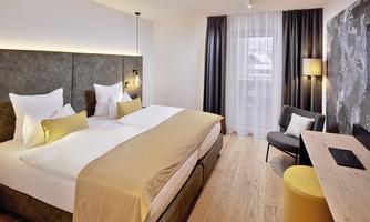 A modern hotel room with a large double bed and bright pillows. The space is friendly and designed in a minimalist style, featuring wooden flooring and soft colors.