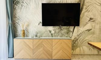 A modern living environment with a television on the wall and an elegant wooden cabinet. The wall is decorated with a palm leaf pattern.