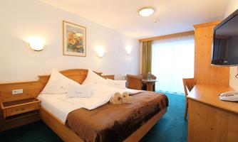 A cozy hotel room with a large bed and wooden furniture. The room features a desk and a balcony with daylight.