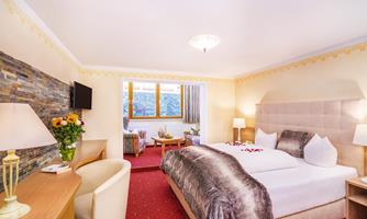 A modern hotel room with a large bed, a desk, and a cozy seating area.  
Large windows let in plenty of light and offer a view outside.