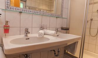 A modern bathroom with a double sink and fresh towels. In the background, a shower enclosure is visible, making the space practical and inviting.