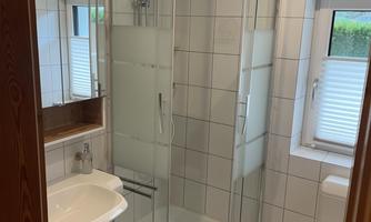 A modern bathroom with a glass shower and bright tiles. There's a sink, a mirror, and a toilet.