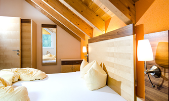 A cozy bedroom with a wooden ceiling and warm colors. The bed is adorned with soft pillows and a bedspread.