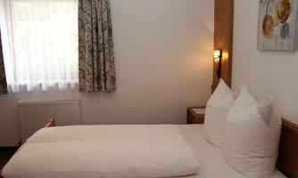A cozy room with a double bed and large, white pillows. The window lets in daylight and a warm atmosphere is created by the wooden details.