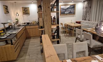 A modern restaurant with wooden details and an inviting atmosphere. There are tables, an open kitchen, and decorations for a cozy dining environment.