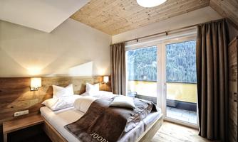 A modern bedroom with wooden decor and large windows. The view overlooks a beautiful landscape and there is a balcony.