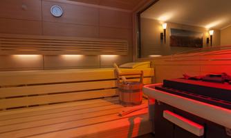 A modern sauna with a wooden bench and bucket. Soft lighting creates a relaxed atmosphere.