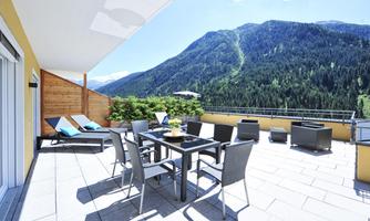 A sunny terrace with modern furniture and a view of the mountains. The space offers an inviting atmosphere amidst nature.