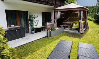A cozy garden area with a pavilion and seating. Two loungers are on the well-maintained lawn, surrounded by plants.