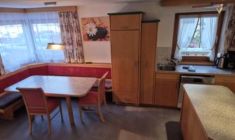 A cozy kitchen with a dining area and a bench. The wooden cabinets and windows create a warm atmosphere.