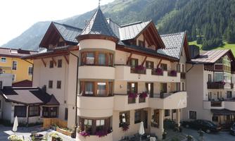 A charming hotel with wooden elements and balconies. Surrounded by mountains and a green landscape.