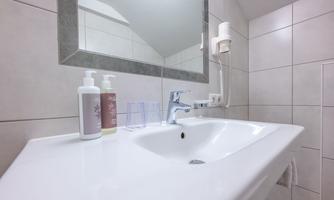A modern bathroom with a clean sink and a large mirror. In the background, personal care products are visible on the shelf.