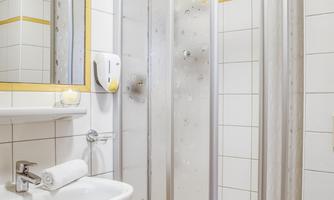 A small bathroom with a shower and a sink. The walls are tiled and the light is bright.