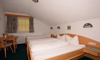 A cozy bedroom with two single beds and pillows. There is a small table and a windowsill with curtains.