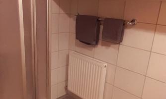 A modern bathroom with a shower cabin. Towels hang on the wall and a green bath rug is on the floor.