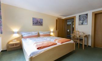 A cozy bedroom with a large double bed and colorful cushions. The room is bright and features a desk as well as modern decoration.