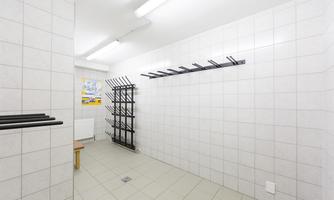 A simple, bright changing room with tiled walls. Coat racks hang on one wall and a table is in the room.