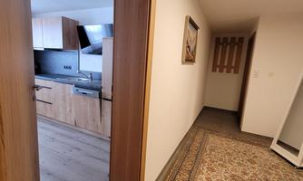 A bright hallway with wooden details and a beautiful carpet. In the background, a modern kitchen is visible.
