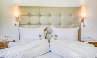 A cozy bedroom with two beds and an elegant headboard design. The walls are light and the lighting creates a pleasant atmosphere.