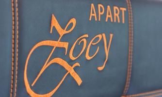 An elegant inscription with the name "Zoey" and the word "APART" in orange text on a blue background. The design conveys a modern and inviting impression.