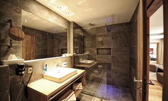 A modern bathroom with a spacious shower and an elegant sink. The walls are clad with gray tiles and the lighting creates a pleasant atmosphere.