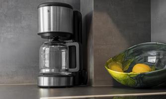A modern coffee machine is on a countertop. Next to it is a colorful bowl with lemons.