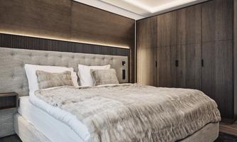 A modern bedroom with a large, comfortable bed and a cozy blanket. The walls are stylishly painted in neutral tones, and there is an elegant wardrobe.