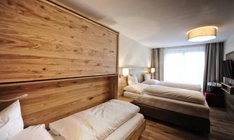 A modern hotel room with wooden accents and two beds. Large windows provide natural daylight and a welcoming atmosphere.