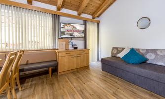 A cozy living space with wooden ceilings and large windows. There is a couch, a table, and modern furniture.