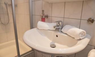 A modern bathroom with a sink and white towels. In the background, there is a shower with a glass partition.