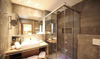 A modern bathroom with a glass shower and a stylish sink. The walls are clad in gray tiles, and there is a large mirror surface.
