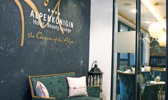 An elegant reception area of the hotel "Alpenkönigin" with a stylish green sofa and modern decor. The walls are creatively designed and invite relaxation.
