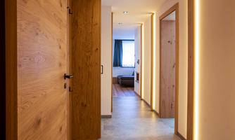 A bright hallway with wooden doors and indirect lighting. At the end of the hallway, there is a window that lets in daylight.