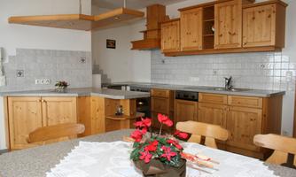 A modern kitchen with wooden cabinets and an elegant table. On the table, there is a blooming plant.