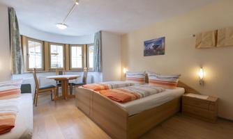 A cozy room with two beds, a table, and chairs.  
Bright walls and large windows create an inviting atmosphere.