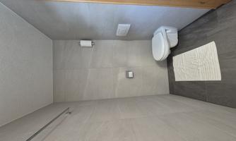A modern bathroom with light gray walls and a white toilet. There is a white rug on the floor.