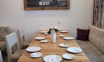 An elegant dining table made of wood with set dishes. In the background hangs a black and white painting of a landscape.