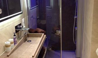 A modern bathroom with a glass shower and stylish blue lights. An elegant sink with a wooden shelf and some bathroom accessories is clearly visible.