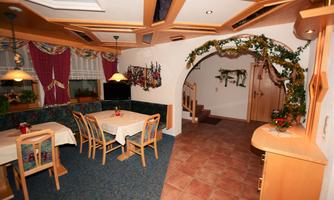 A cozy dining area with tables and chairs. In the background, a staircase leads to another room, and there are decorative plants.