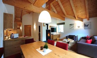A cozy apartment with wooden ceilings and modern furniture. The space is bright and inviting, featuring a large dining table and a living area.