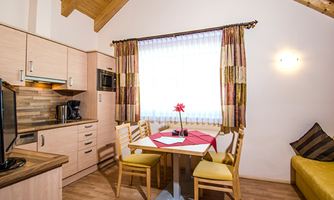 A cozy kitchen corner with a table and chairs. Light-filled windows with curtains and a modern interior create an inviting atmosphere.